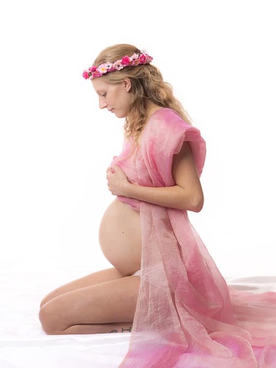 Gravidfotografering - gravid kvinna sitter p&aring; kn&auml; och tittar p&aring; sin mage
